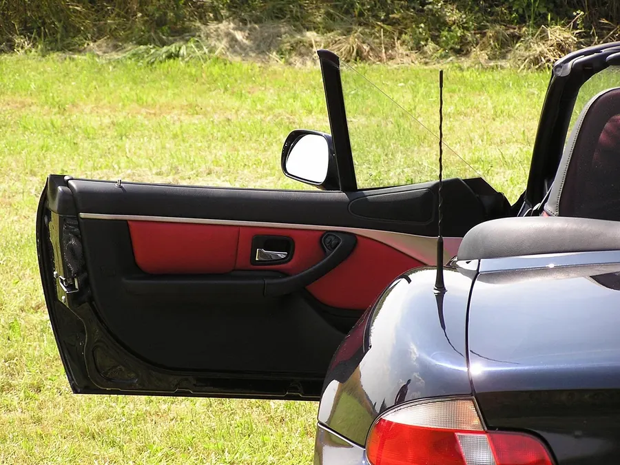 Open door of a roadster showing a red and black door panel beside the driver seat