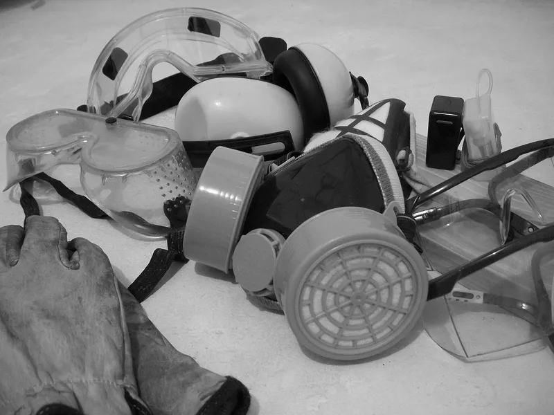 Safety goggles, glasses, respirator, ear muffs and a work glove on a floor