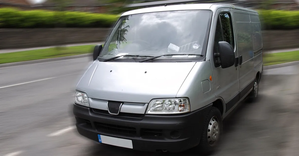 Silver low-roof cargo van driving along a street, front three-quarter view