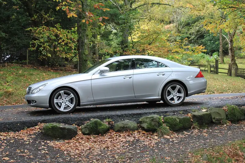 Silver sedan parked beside a road with autumn trees behind it