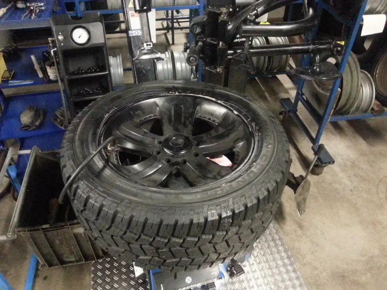 Tire mounted on a tire-changing machine in a service bay with wheels racked behind it