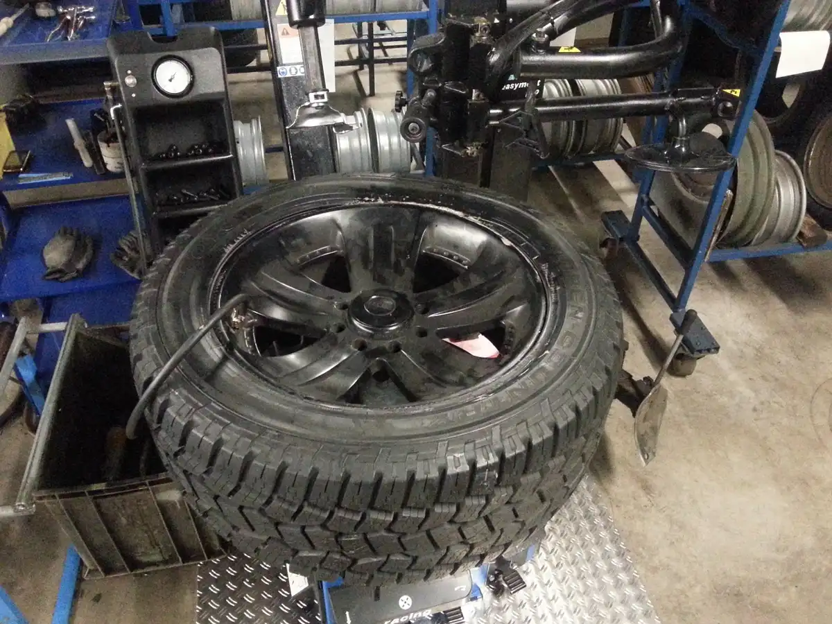 Tire mounted on a tire-changing machine in a service bay with wheels racked behind it