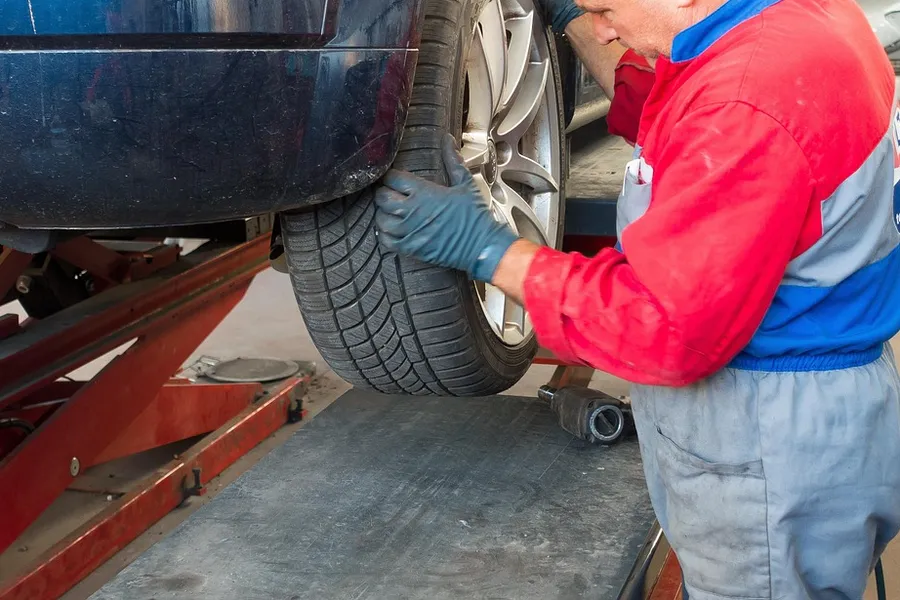 Technician in work gloves handling a car wheel on a service lift