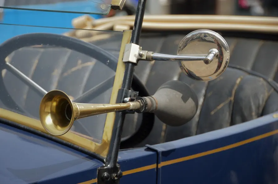 Brass bulb horn and round side mirror on the windshield frame of a vintage open car