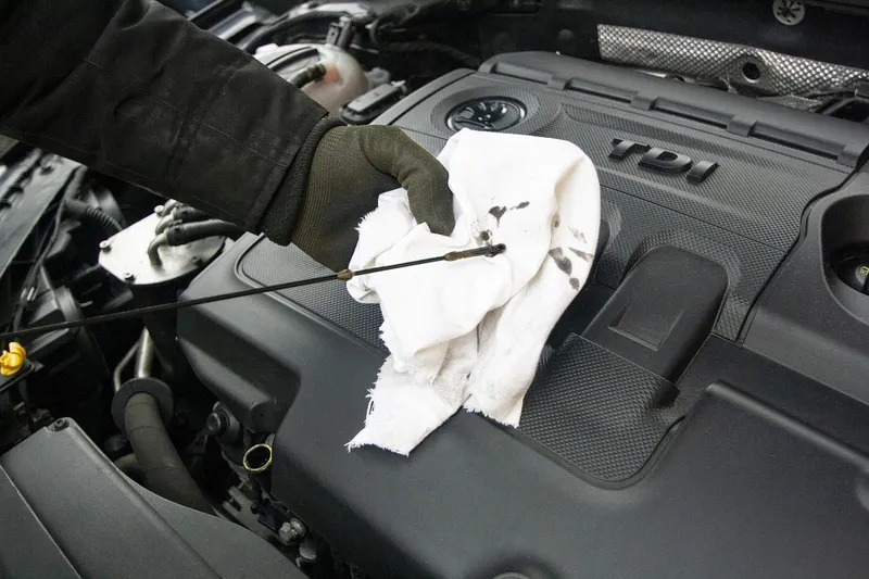 Technician wiping an engine oil dipstick with a rag to check the oil level