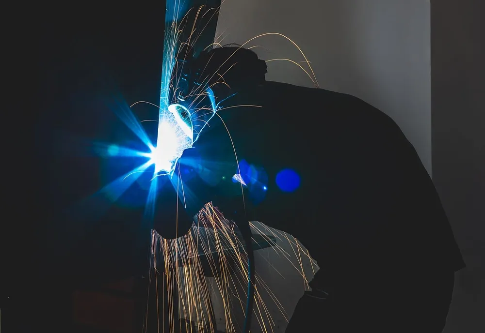 Welder in a dark workshop with a bright welding arc and sparks