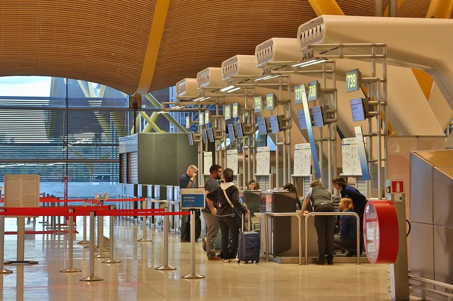Travelers at airport check-in counters under a curved wooden ceiling