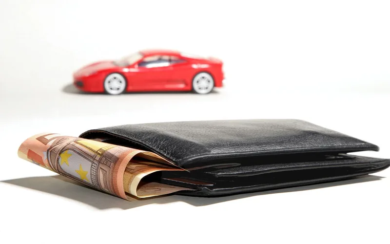 Car keys and banknotes beside auto financing paperwork showing monthly loan costs
