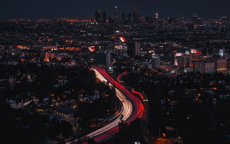 Highway light trails leading toward a city skyline at night