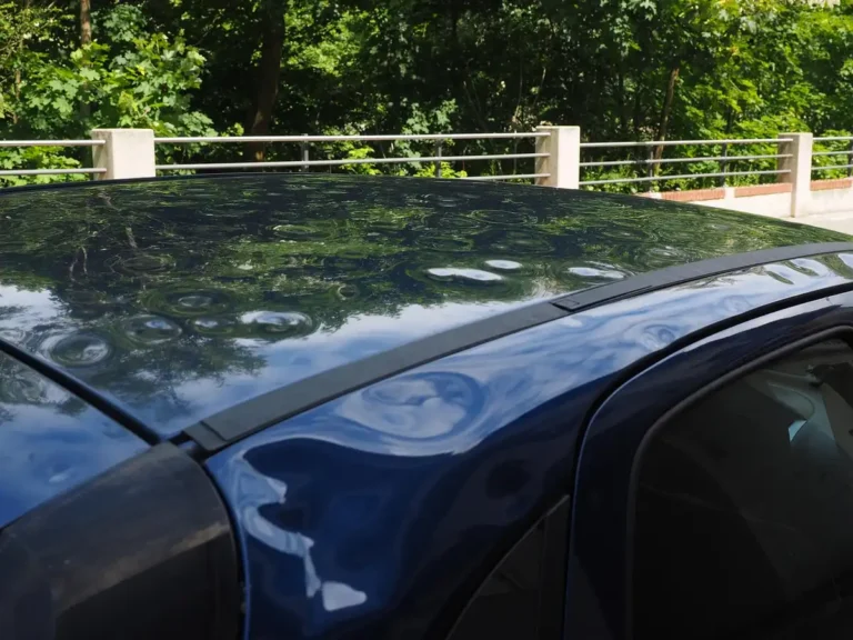 Dents in the roof and door pillar of a dark blue car, with tree reflections showing the uneven surface