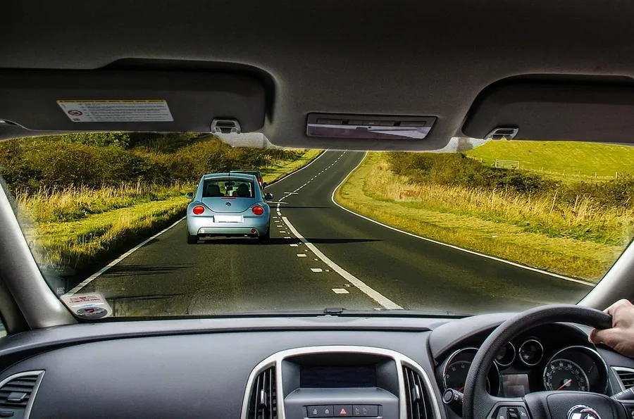 View through a car windshield of a winding country road with a car ahead