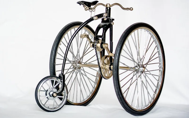 Small model of a late-1800s bicycle with wire wheels, a chain and a small front wheel