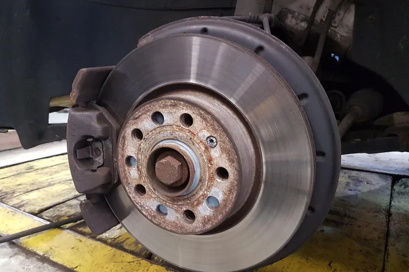 Brake rotor with a rusty hub and caliper on a car lifted in a garage