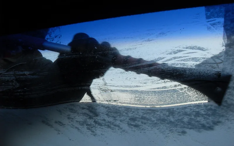 gloved hand using an ice scraper to remove frost from a car windshield gloved hand using an ice scraper to remove frost from a car windshield