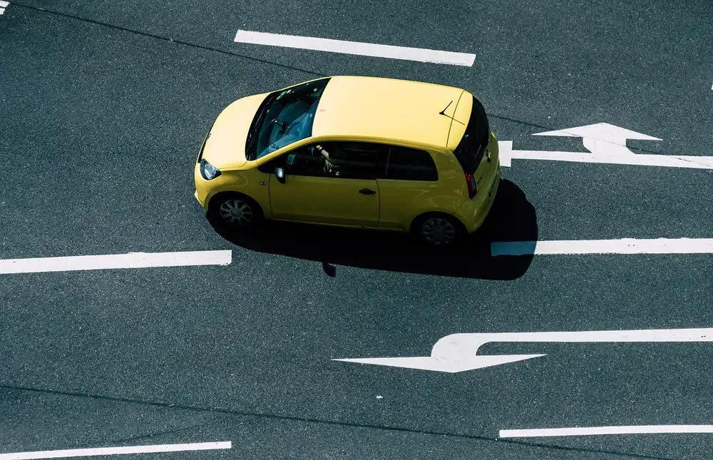 Small yellow car seen from above on a road with painted lane arrows