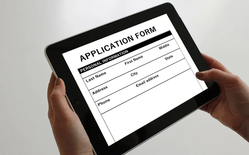 Hands holding a tablet that shows a blank application form
