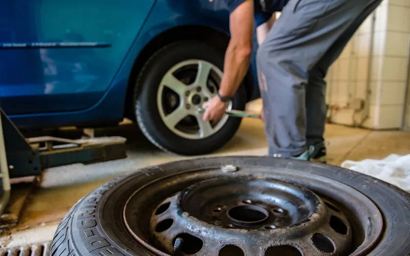 Technician loosening wheel nuts on a car in a garage with a spare wheel in the foreground