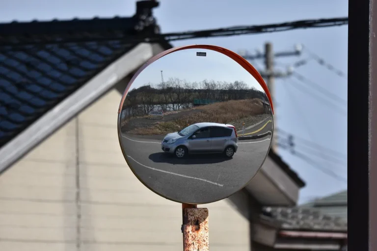 Round convex road mirror on a pole reflecting a silver hatchback and the road