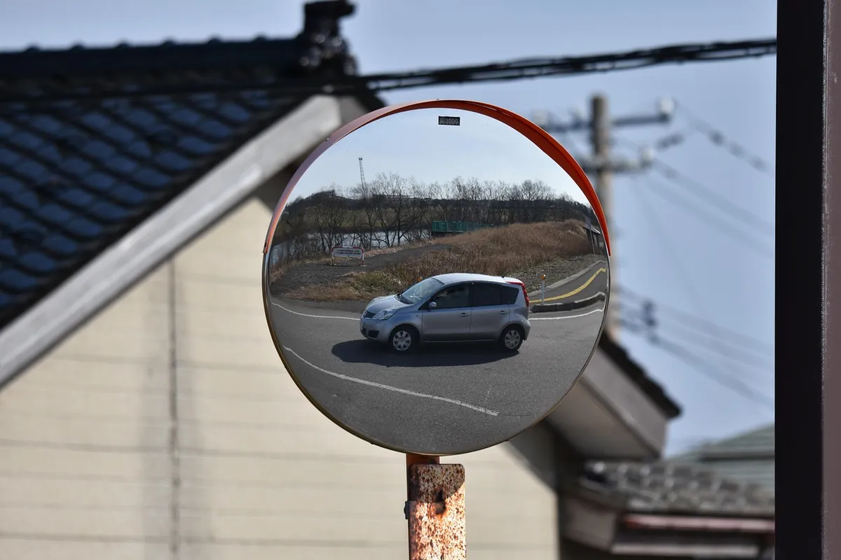 Round convex road mirror on a pole reflecting a silver hatchback and the road
