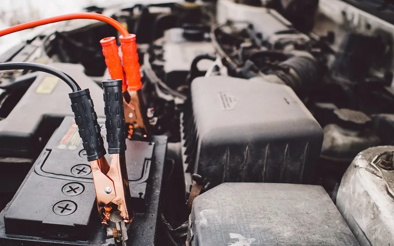 Jumper cable clamp connected to a car battery terminal under the hood