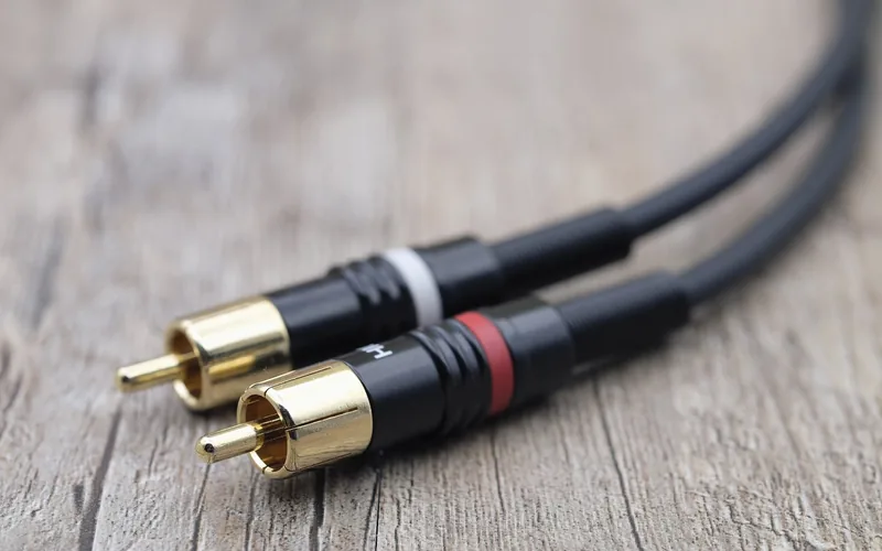 Two RCA plugs connected end to end on a wood surface, the audio cable path used in car audio systems