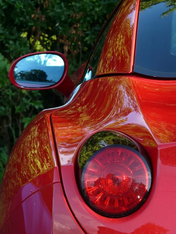 Rear corner of a red car showing a round tail light and the side mirror