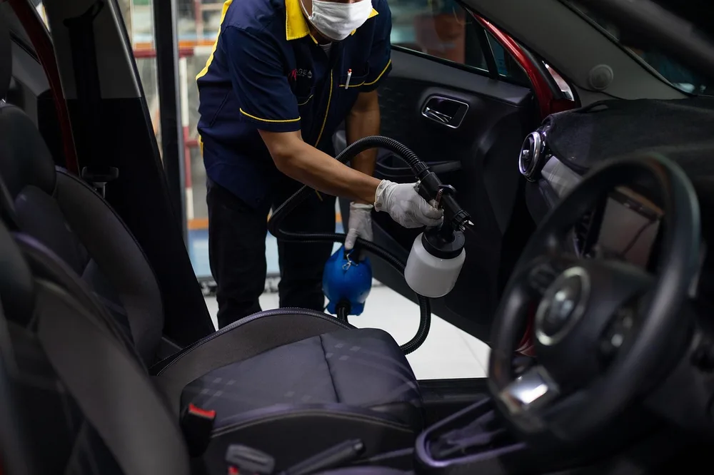Technician in a face mask and gloves spraying cleaner inside a car cabin