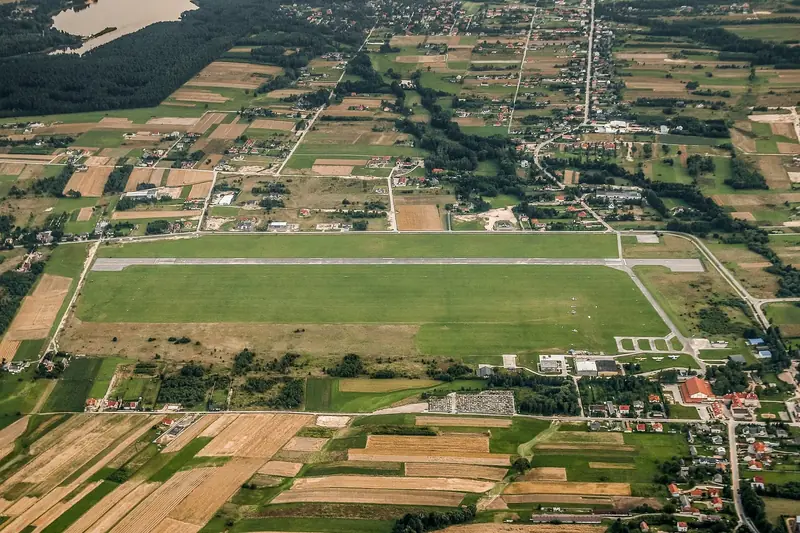 Aerial view of a grass airfield with a paved runway surrounded by farmland and villages