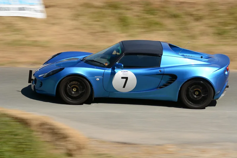 Blue Lotus Elise sports car with a race number driving along a road