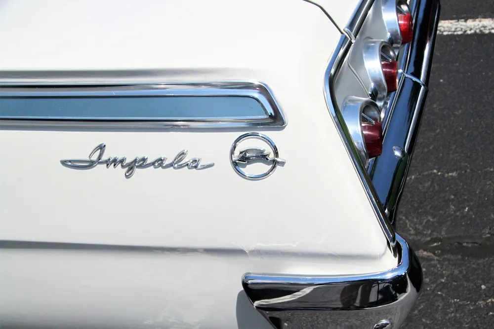 Chrome Impala script badge and crossed-flags emblem on the rear quarter of a white classic Chevrolet