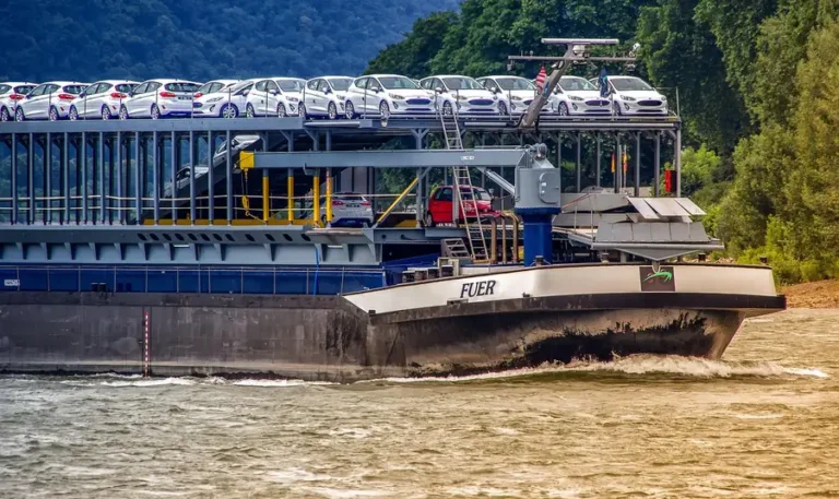 Vessel carrying a deck of new white cars on a river