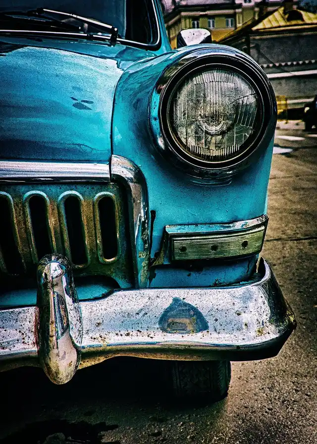 Front end of a vintage blue car with a chrome bumper and round headlight