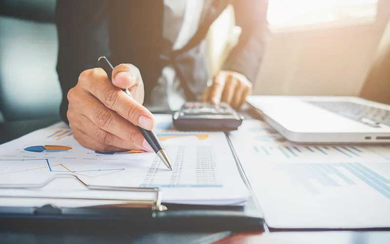 Person reviewing financial charts with a pen and calculator at a desk