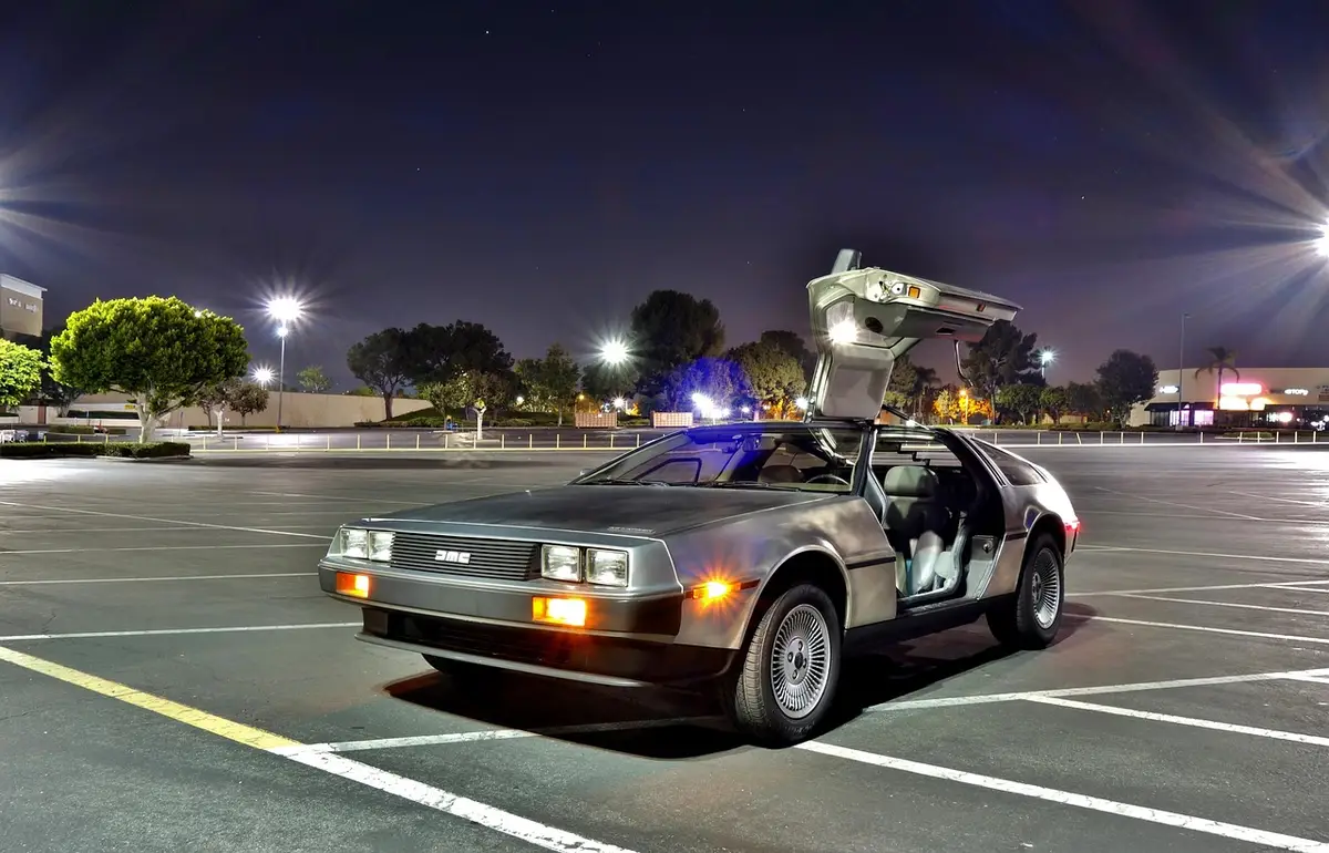 A DeLorean DMC-12 with its gull-wing door raised in a parking lot at night