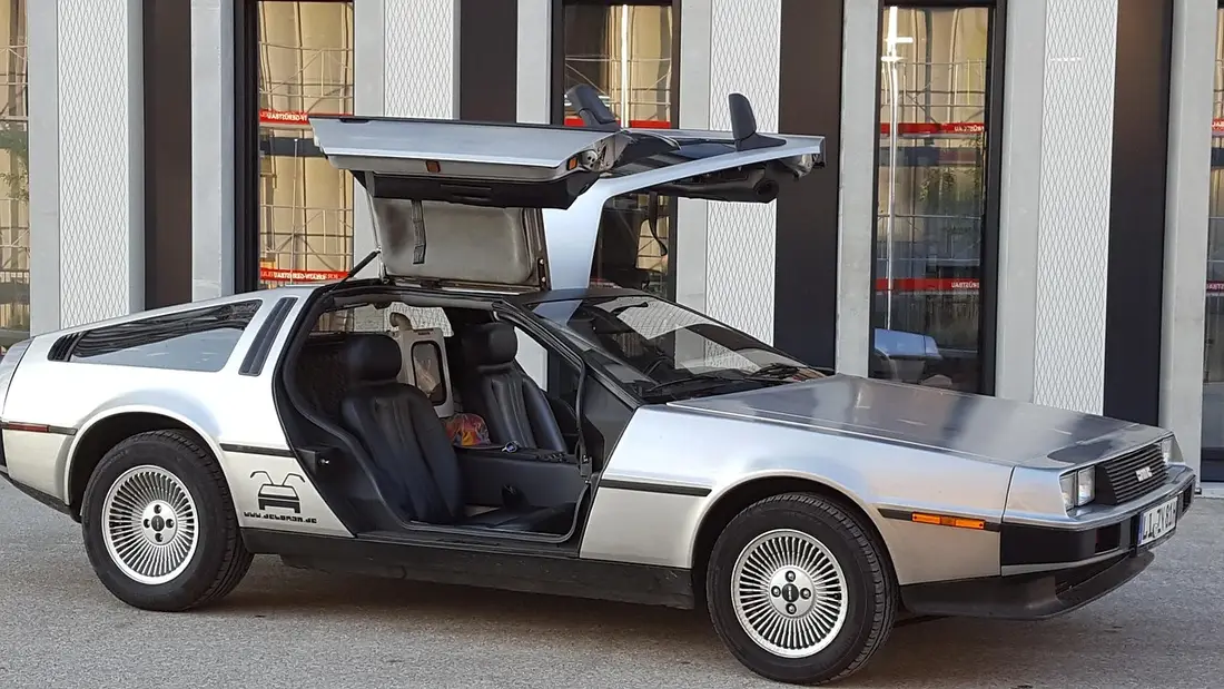 A DeLorean DMC-12 with both gull-wing doors open, seen from the side