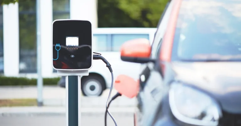 Electric car parked beside a wall-mounted charging post with a charging cable plugged in