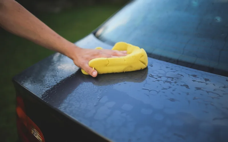 Hand wiping a wet car body panel with a yellow sponge before scratch repair Hand wiping a wet car body panel with a yellow sponge before scratch repair