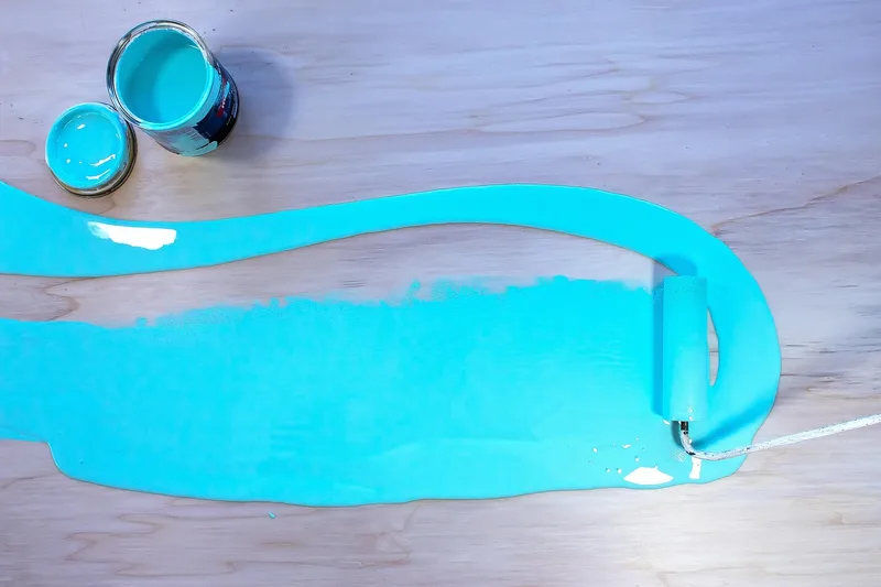 Paint roller spreading turquoise coating across a flat wooden surface