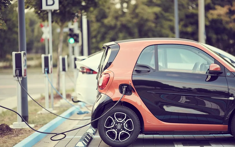 Small electric car plugged into a roadside charging post in a row of charging points