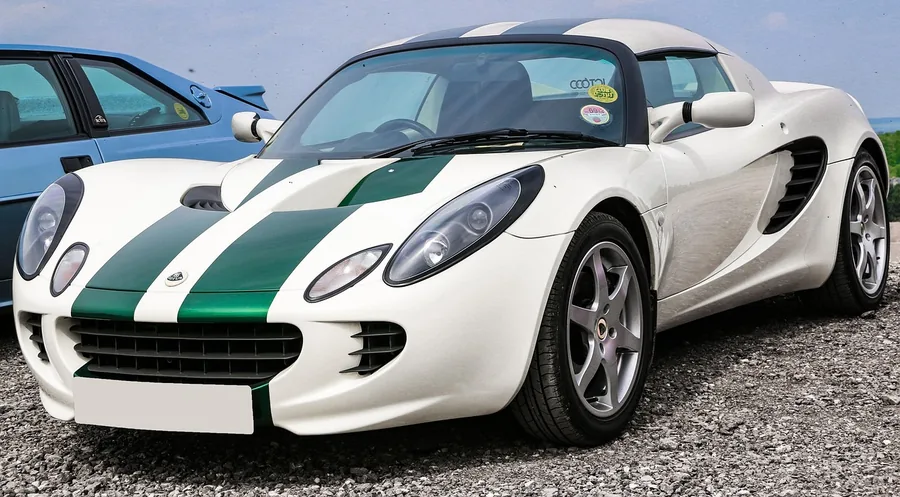White Lotus Elise sports car with green racing stripes parked on gravel