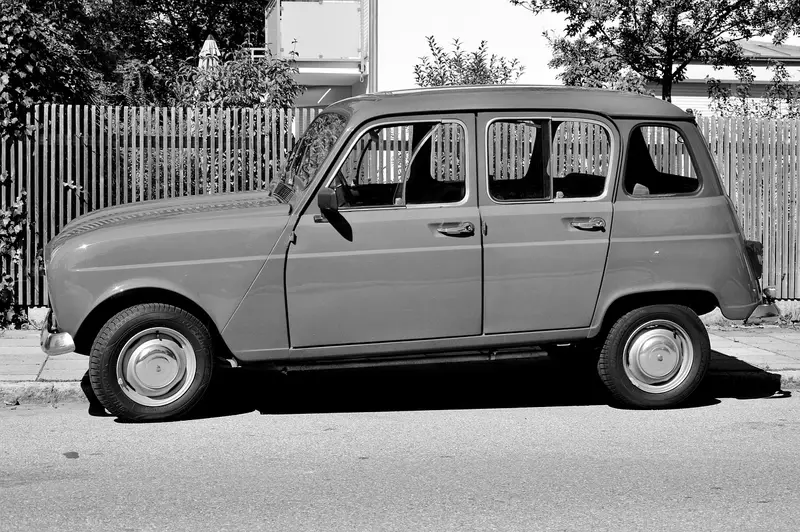 Classic small hatchback parked beside a wooden fence, black and white photo