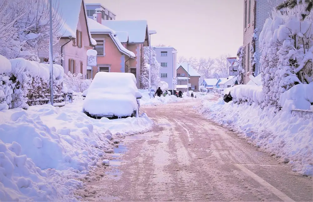 Snowy residential street with a parked car covered in snow