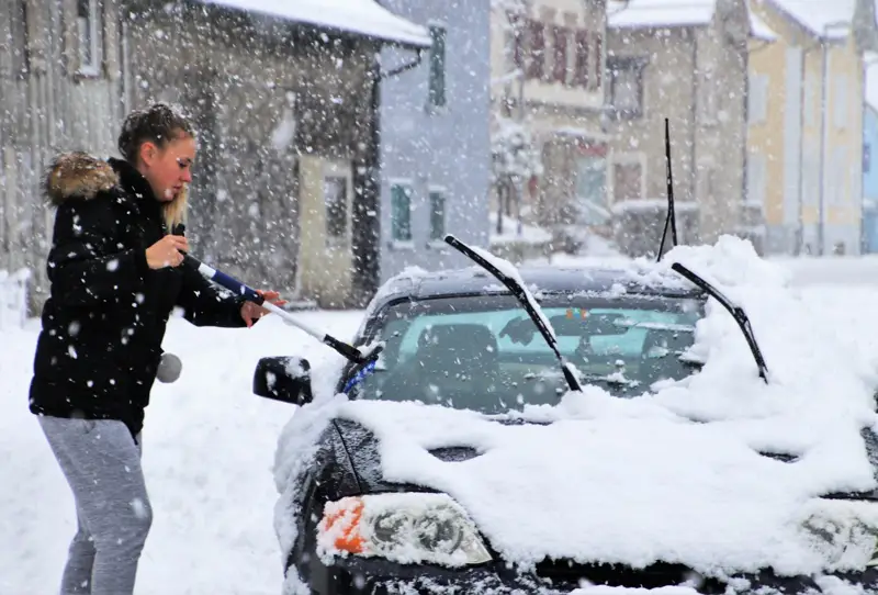 Woman using a snow brush to clear snow from a car windshield