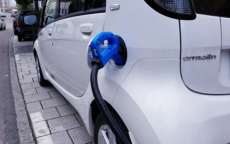Electric car plugged into a public charging station beside a highway Electric car plugged into a public charging station beside a highway