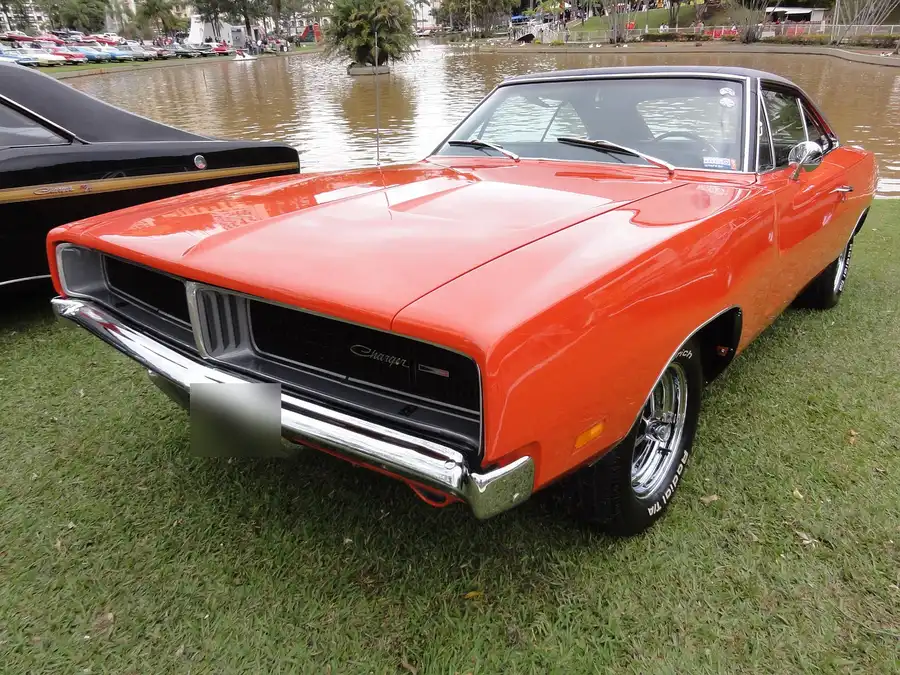 Orange 1969 Dodge Charger with a black vinyl roof parked on grass at a car show