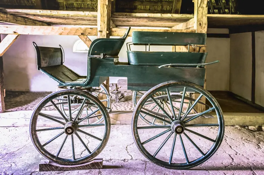 Green horse-drawn carriage with spoked wheels parked inside a barn