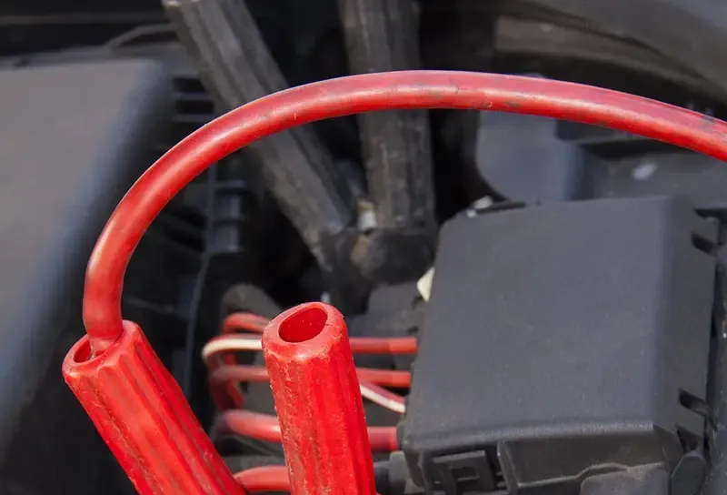 Red jumper cable clamp attached to a car battery terminal under the hood