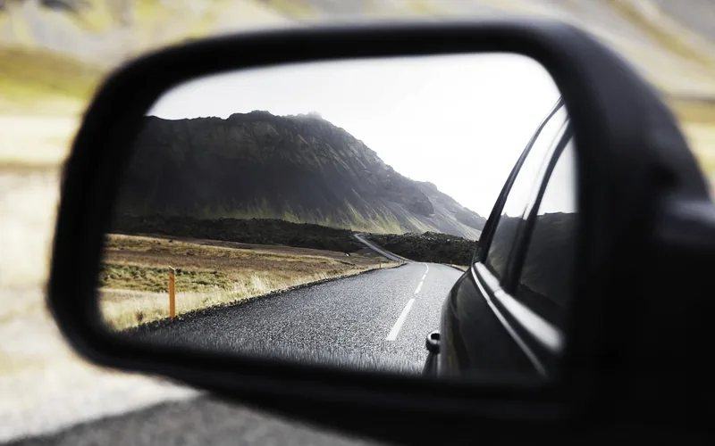 Side mirror showing a winding road and a mountain behind a car
