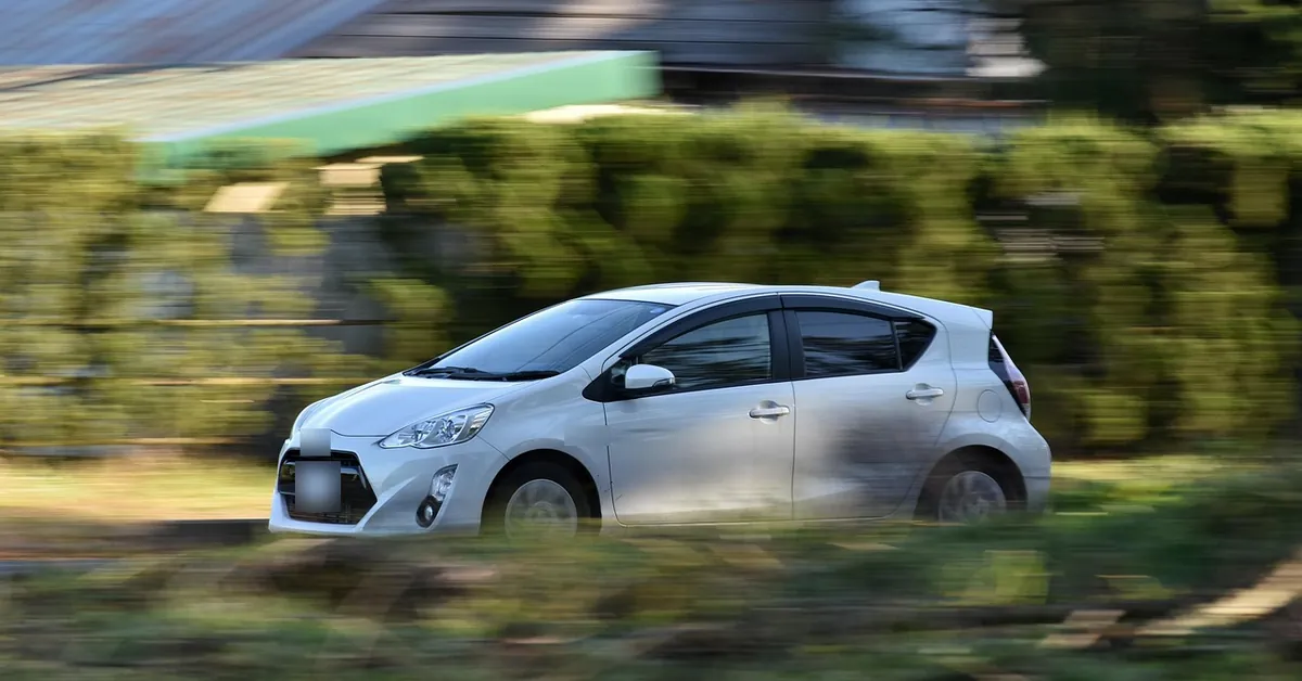 Silver hatchback car driving along a road past a hedge, shown with motion blur