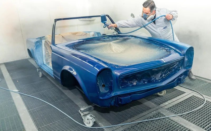 Painter using a spray gun to apply single-stage acrylic enamel paint to a car body Painter using a spray gun to apply single-stage acrylic enamel paint to a car body